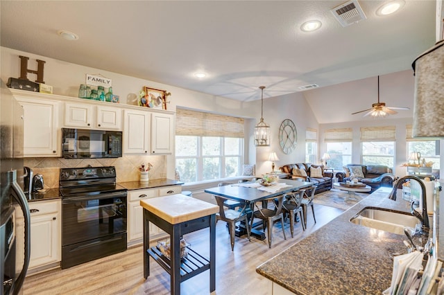 kitchen featuring lofted ceiling, sink, hanging light fixtures, dark stone countertops, and black appliances