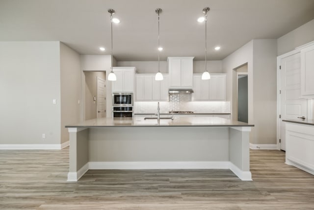 1017 Daisy Way, Crowley, TX 76036 - kitchen with a kitchen island with sink, decorative backsplash, light wood finished floors, under cabinet range hood, and white cabinetry