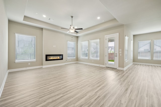 1017 Daisy Way, Crowley, TX 76036 - unfurnished living room with a raised ceiling, light wood-style flooring, a glass covered fireplace, baseboards, and ceiling fan