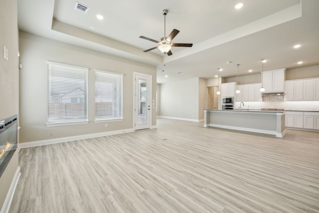 1017 Daisy Way, Crowley, TX 76036 - unfurnished living room featuring ceiling fan, recessed lighting, light wood-style floors, a tray ceiling, and baseboards