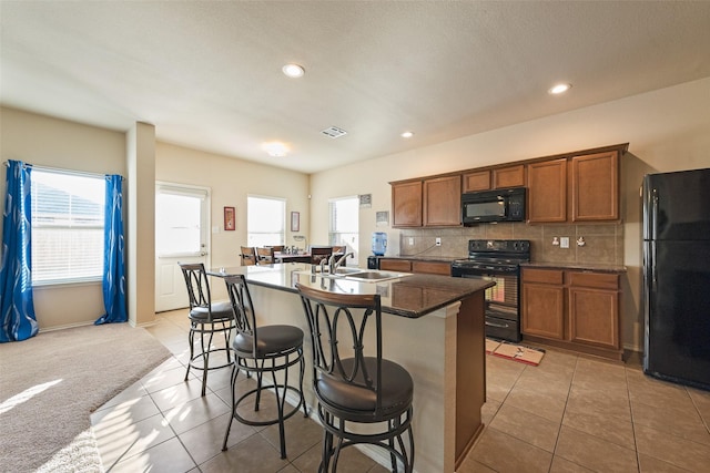 kitchen with sink, a breakfast bar area, light carpet, an island with sink, and black appliances