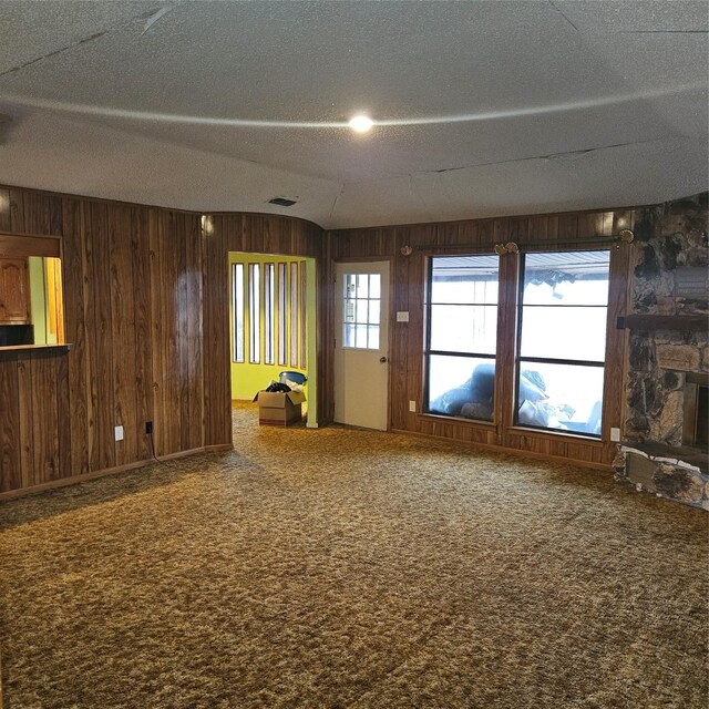 134 Hollie Dr, Red Oak, TX 75154 - spare room featuring wooden walls, carpet flooring, a stone fireplace, and a textured ceiling