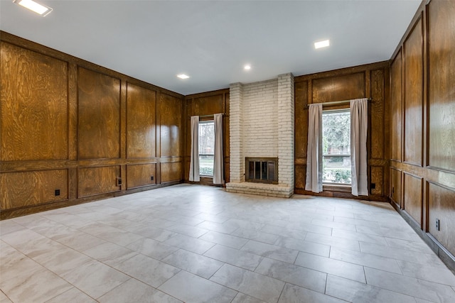 unfurnished living room with plenty of natural light, a fireplace, and wood walls