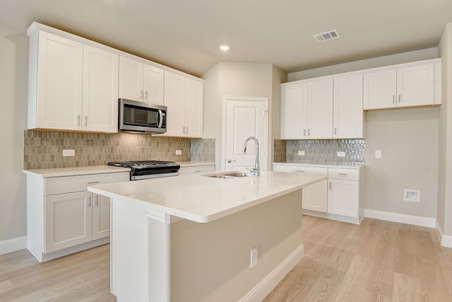 kitchen with sink, stainless steel appliances, white cabinets, and a center island with sink