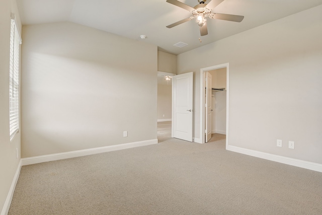 unfurnished bedroom featuring vaulted ceiling, a spacious closet, ceiling fan, light carpet, and a closet