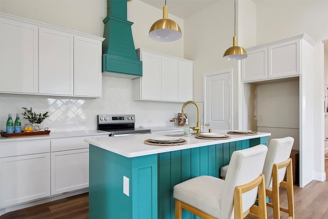 kitchen featuring premium range hood, pendant lighting, white cabinets, a kitchen island with sink, and stainless steel electric range