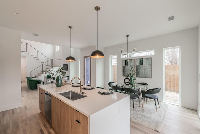 kitchen featuring sink, dishwasher, hanging light fixtures, an island with sink, and light wood-type flooring