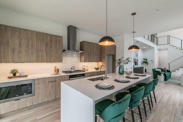 kitchen featuring black microwave, sink, a kitchen bar, hanging light fixtures, and wall chimney exhaust hood