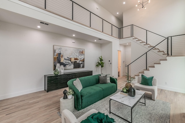 living room with a towering ceiling, an inviting chandelier, and light hardwood / wood-style floors