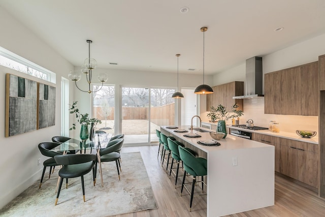 kitchen with a kitchen island with sink, pendant lighting, wall chimney exhaust hood, and a kitchen bar