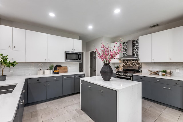 kitchen with wall chimney exhaust hood, white cabinetry, a center island, appliances with stainless steel finishes, and gray cabinets