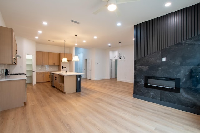 kitchen featuring a kitchen island with sink, decorative light fixtures, tasteful backsplash, and light hardwood / wood-style floors