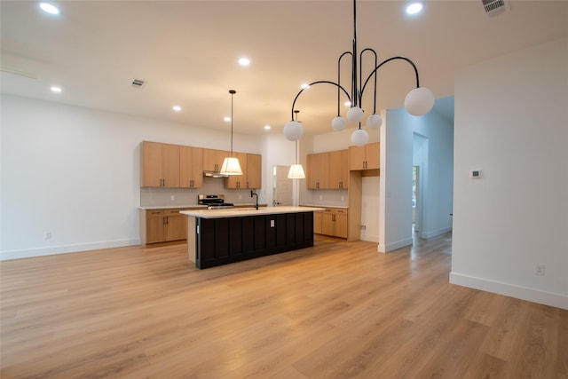 kitchen featuring light brown cabinetry, decorative light fixtures, stainless steel electric range, a center island with sink, and light hardwood / wood-style flooring