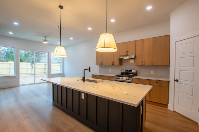 kitchen with pendant lighting, sink, a kitchen island with sink, backsplash, and stainless steel gas range oven