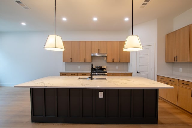 kitchen with decorative light fixtures, light brown cabinetry, and a kitchen island with sink