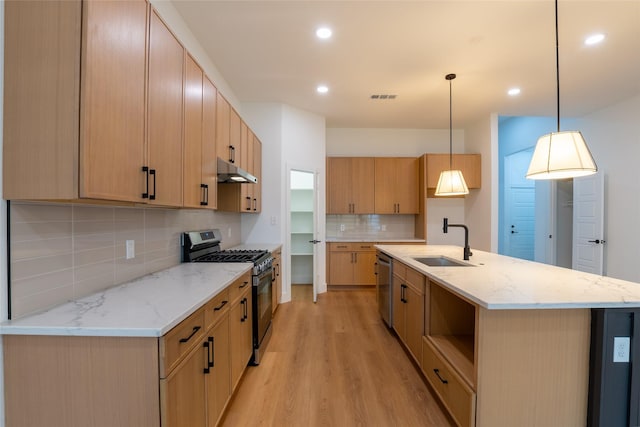 kitchen with pendant lighting, sink, a kitchen island with sink, stainless steel appliances, and light wood-type flooring