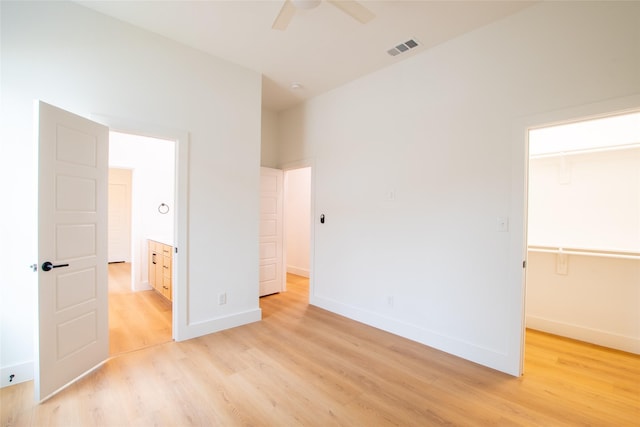 unfurnished bedroom featuring ceiling fan, a spacious closet, and light wood-type flooring