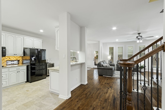 kitchen featuring white cabinets, decorative backsplash, black fridge, ceiling fan, and light stone countertops