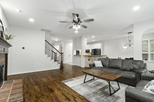 living room featuring a brick fireplace, hardwood / wood-style flooring, and ceiling fan with notable chandelier