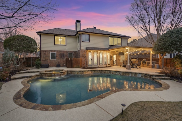 pool at dusk with an in ground hot tub and a patio