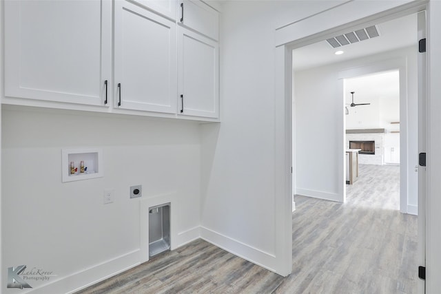 washroom with light hardwood / wood-style flooring, cabinets, washer hookup, a fireplace, and hookup for an electric dryer