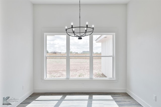 unfurnished dining area featuring wood-type flooring and an inviting chandelier