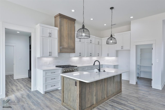 kitchen featuring sink, decorative light fixtures, a center island with sink, light wood-type flooring, and white cabinets