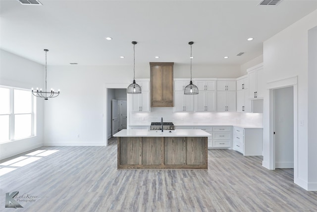 kitchen featuring sink, hanging light fixtures, an island with sink, and white cabinets