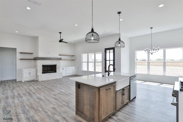 kitchen featuring sink, stainless steel appliances, a center island with sink, a brick fireplace, and ceiling fan with notable chandelier