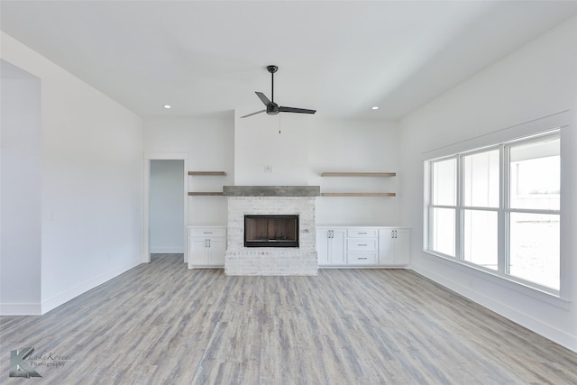 unfurnished living room featuring a brick fireplace, a healthy amount of sunlight, ceiling fan, and light hardwood / wood-style floors