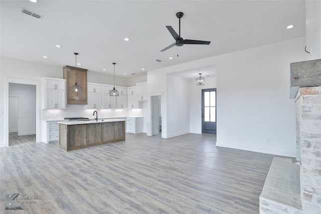 kitchen with ceiling fan with notable chandelier, pendant lighting, white cabinetry, a spacious island, and light hardwood / wood-style flooring