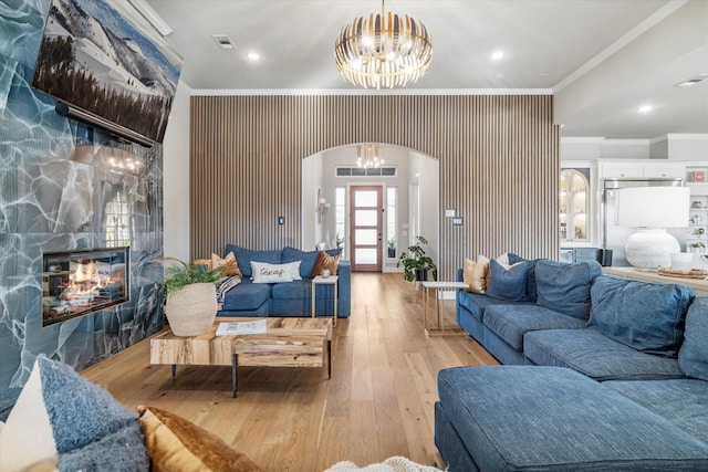 living room with an inviting chandelier, crown molding, a fireplace, and light hardwood / wood-style flooring