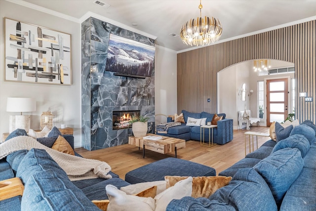 living room with hardwood / wood-style flooring, ornamental molding, an inviting chandelier, and a fireplace