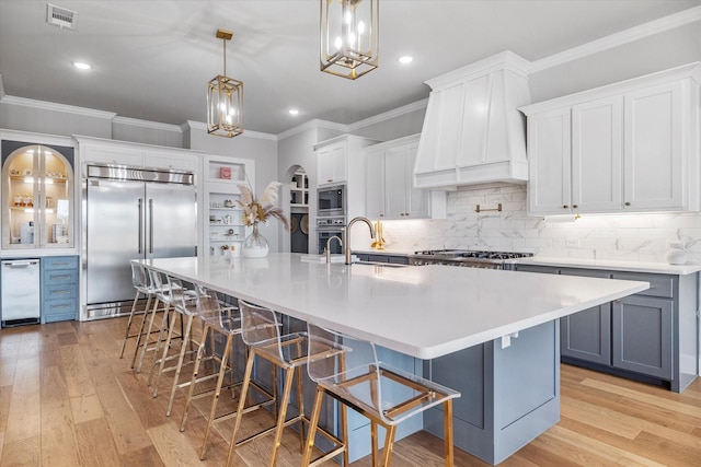 kitchen featuring a breakfast bar, decorative light fixtures, white cabinetry, built in appliances, and a spacious island