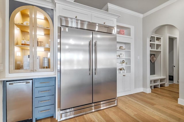 kitchen featuring white cabinetry, stainless steel appliances, ornamental molding, built in shelves, and light wood-type flooring