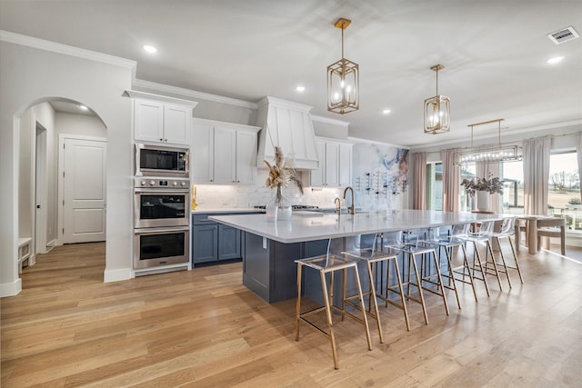 kitchen with blue cabinetry, a kitchen bar, white cabinetry, appliances with stainless steel finishes, and pendant lighting