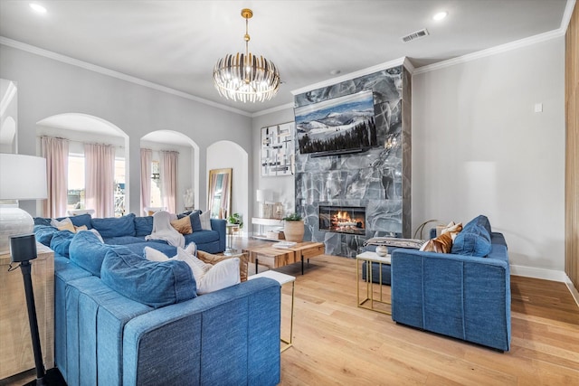 living room featuring a notable chandelier, crown molding, light hardwood / wood-style flooring, and a premium fireplace