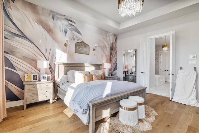 bedroom featuring connected bathroom, a chandelier, and light hardwood / wood-style flooring