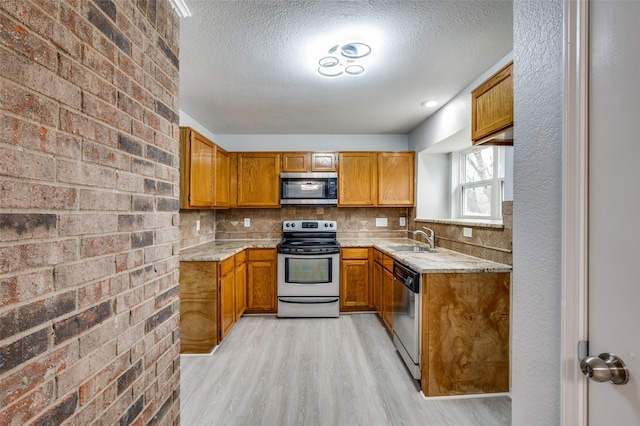 kitchen with sink, light hardwood / wood-style flooring, backsplash, stainless steel appliances, and a textured ceiling