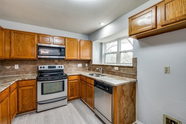 kitchen featuring stainless steel appliances, sink, light wood-type flooring, and decorative backsplash