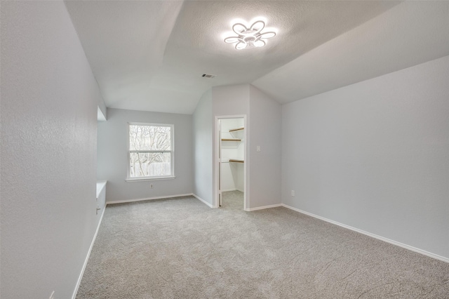 bonus room featuring lofted ceiling, light colored carpet, and a textured ceiling