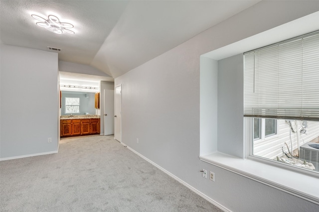 corridor with light colored carpet, lofted ceiling, sink, and a textured ceiling