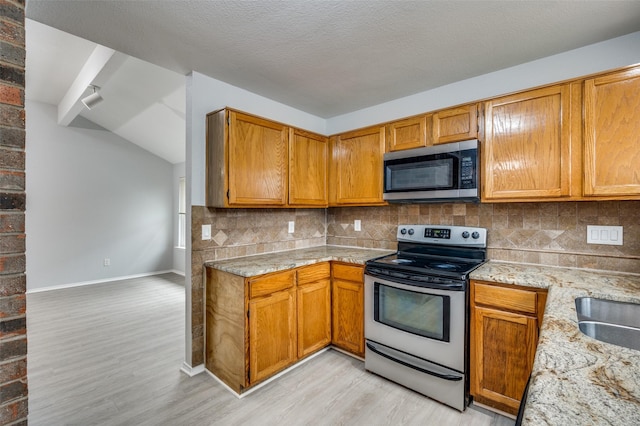 kitchen featuring vaulted ceiling, light wood-type flooring, appliances with stainless steel finishes, light stone countertops, and backsplash