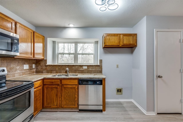 kitchen featuring appliances with stainless steel finishes, sink, backsplash, a textured ceiling, and light hardwood / wood-style flooring