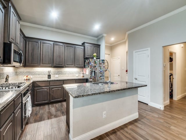 kitchen with a sink, wood finished floors, stainless steel appliances, stone counters, and decorative backsplash