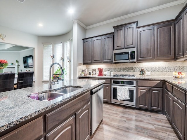 kitchen with light stone countertops, a sink, dark brown cabinetry, appliances with stainless steel finishes, and light wood-type flooring