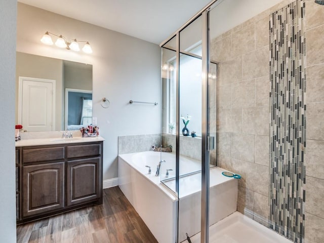 full bath featuring vanity, wood finished floors, baseboards, a stall shower, and a bath