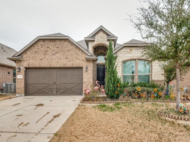 french country home with brick siding, an attached garage, central AC unit, stone siding, and driveway