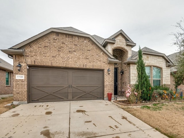 french country inspired facade with stone siding, brick siding, concrete driveway, and an attached garage