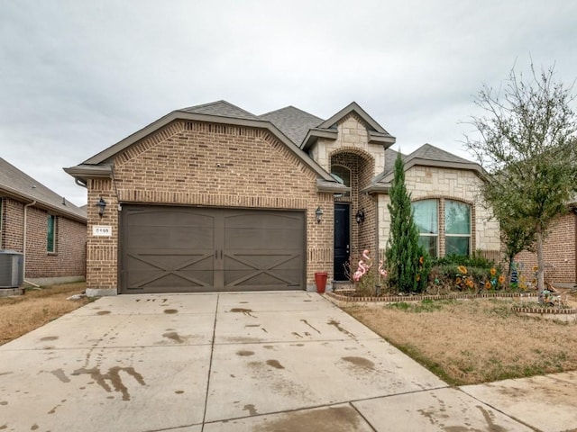 french country style house with concrete driveway, central air condition unit, a garage, and brick siding